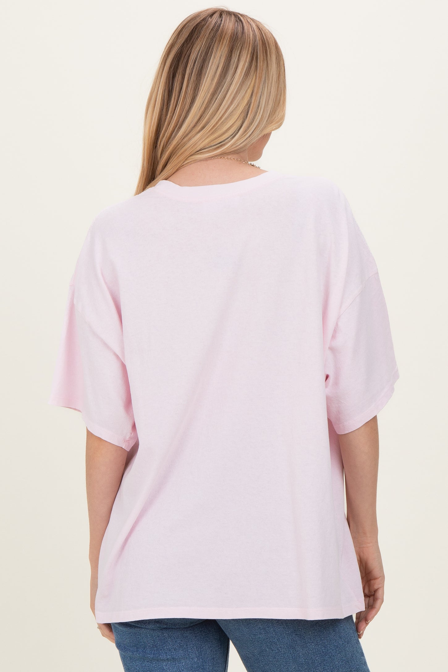 woman wearing a light pink oversized t-shirt viewed from the back with casual styling and rolled sleeves