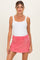 woman wearing a white tank bodysuit and a pink maternity mini skirt with pockets, showing her baby bump