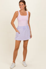 woman wearing a light pink tank bodysuit and a lavender skort with pockets, standing on a neutral background