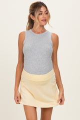 woman wearing a gray sleeveless maternity top and a yellow maternity skirt, showcasing her baby bump