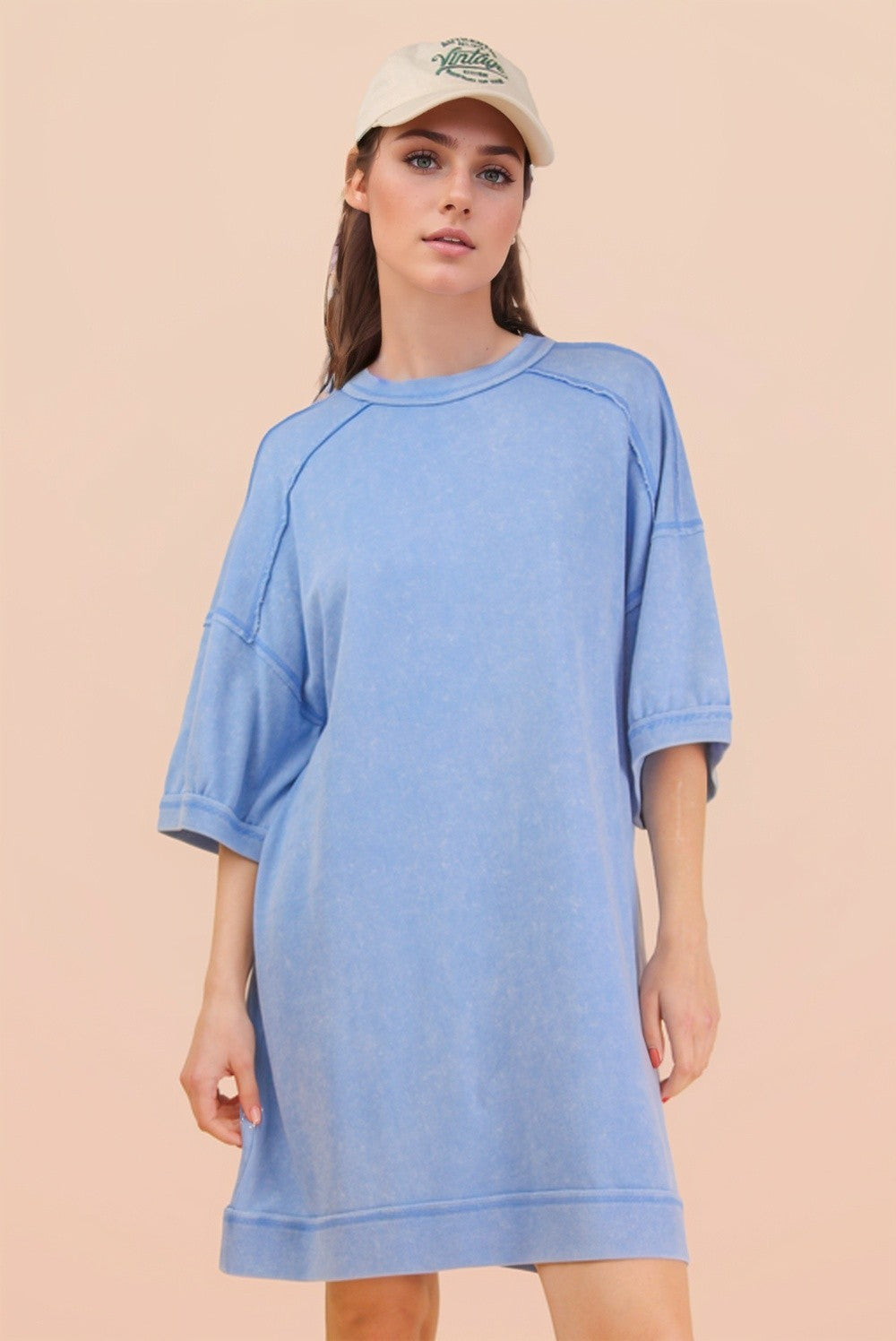 woman wearing a light blue oversized t-shirt dress with short sleeves and a cap