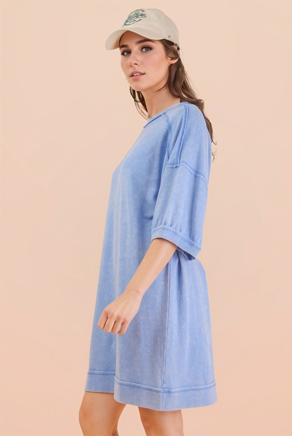 woman wearing a light blue oversized sweatshirt dress with short sleeves and a relaxed fit, styled with a beige cap