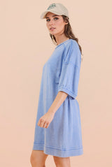 woman wearing a light blue oversized sweatshirt dress with short sleeves and a relaxed fit, styled with a beige cap