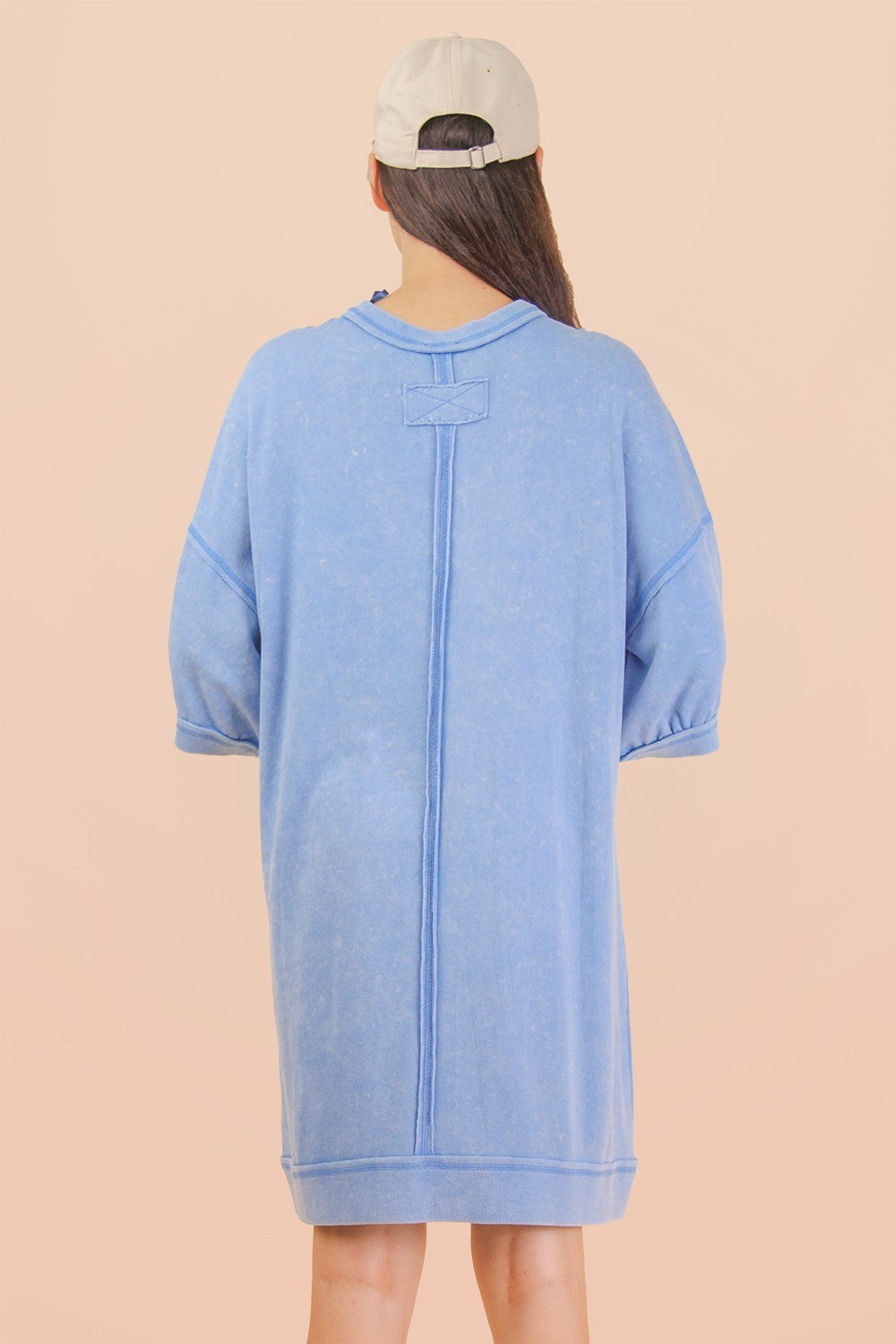 woman wearing a light blue oversized sweatshirt dress with short sleeves and a relaxed fit, seen from the back