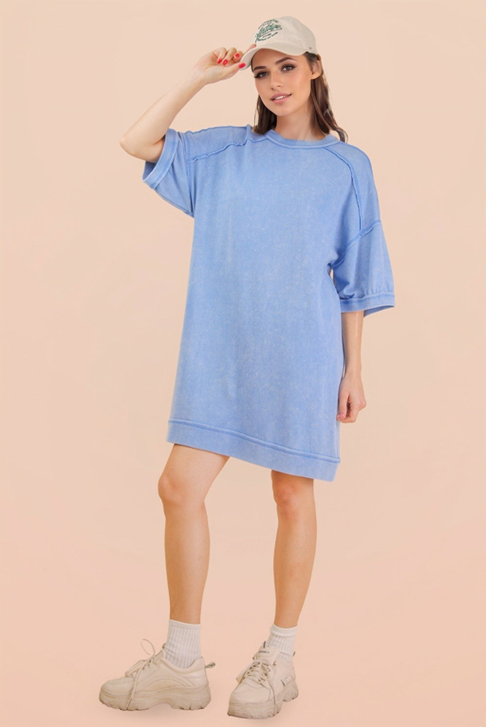 woman wearing a light blue oversized t-shirt dress with short sleeves and a baseball cap