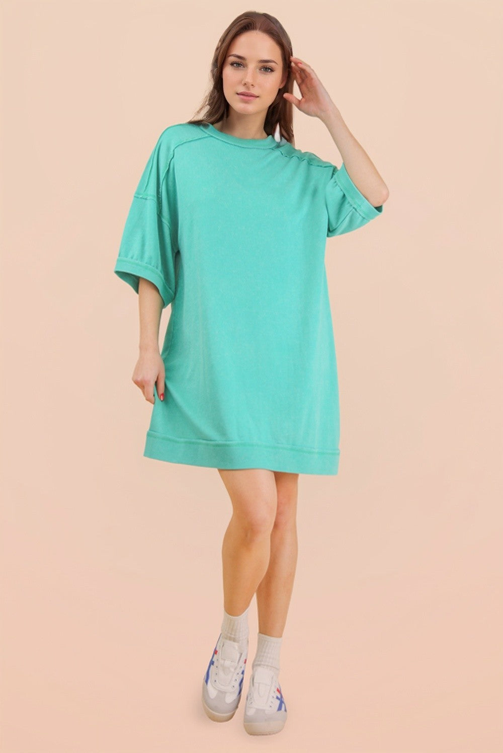 woman wearing a mint green oversized t-shirt dress with short sleeves and a relaxed fit, standing in white sneakers