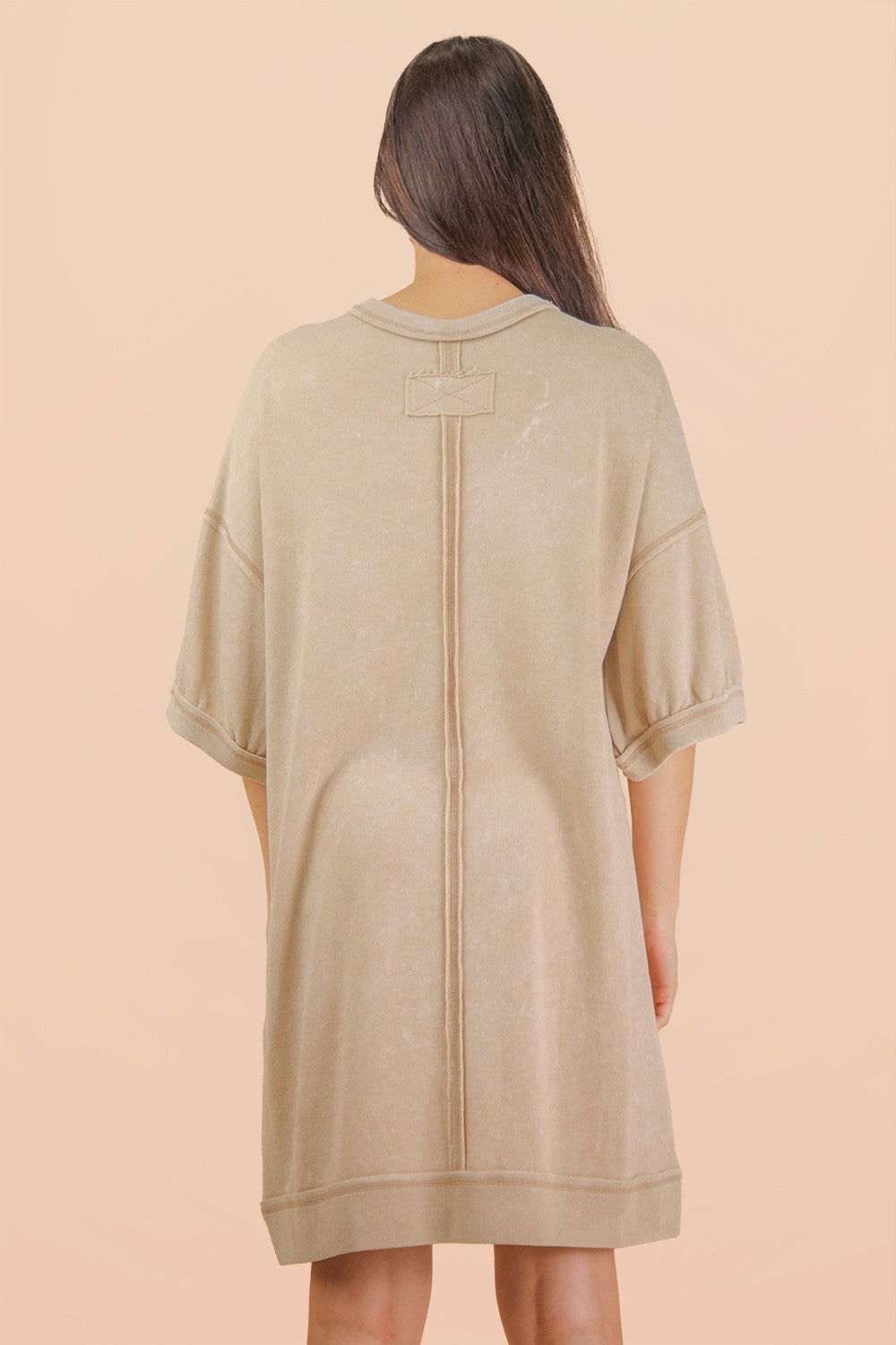 woman wearing a beige oversized sweatshirt dress with a simple back design and short sleeves