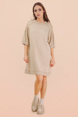 woman wearing a beige oversized sweatshirt dress with short sleeves and a relaxed fit, paired with light sneakers