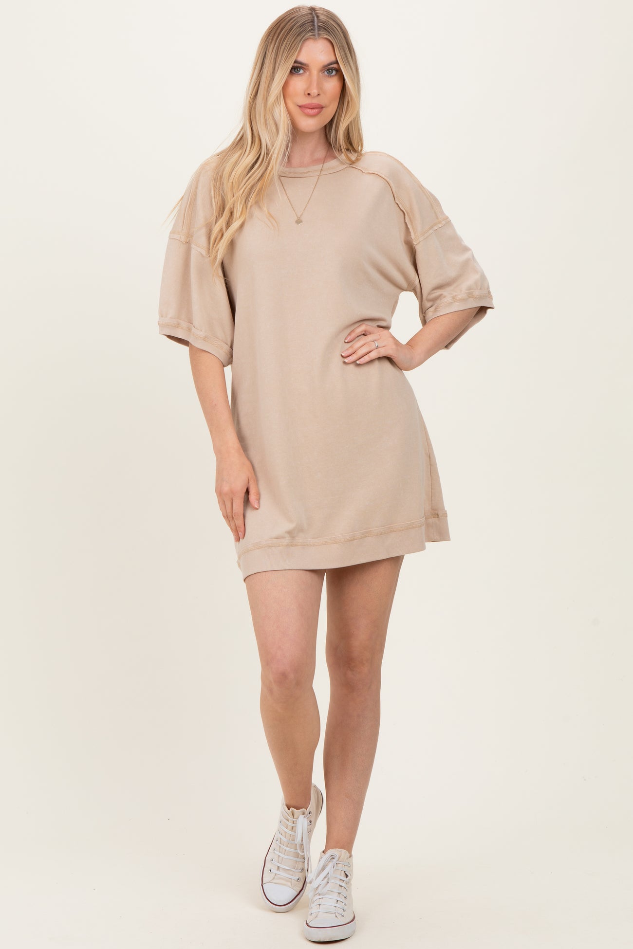 woman wearing a beige oversized sweater dress with short sleeves and white sneakers