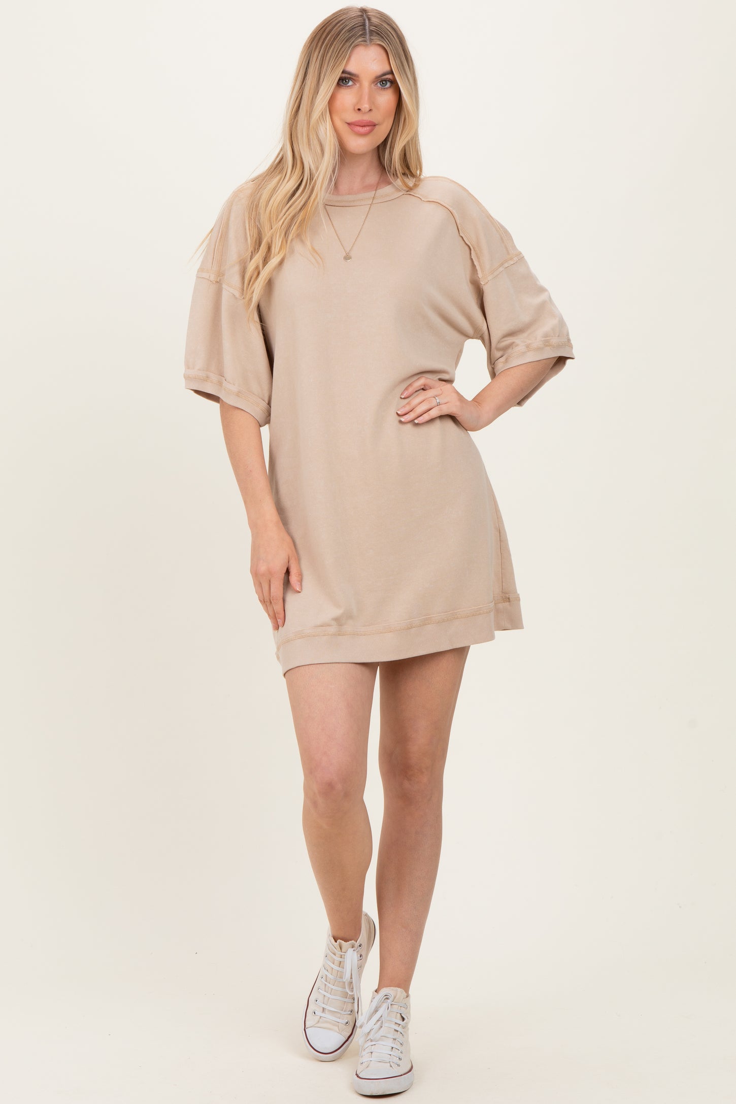 woman wearing a beige oversized sweater dress with short sleeves and white sneakers