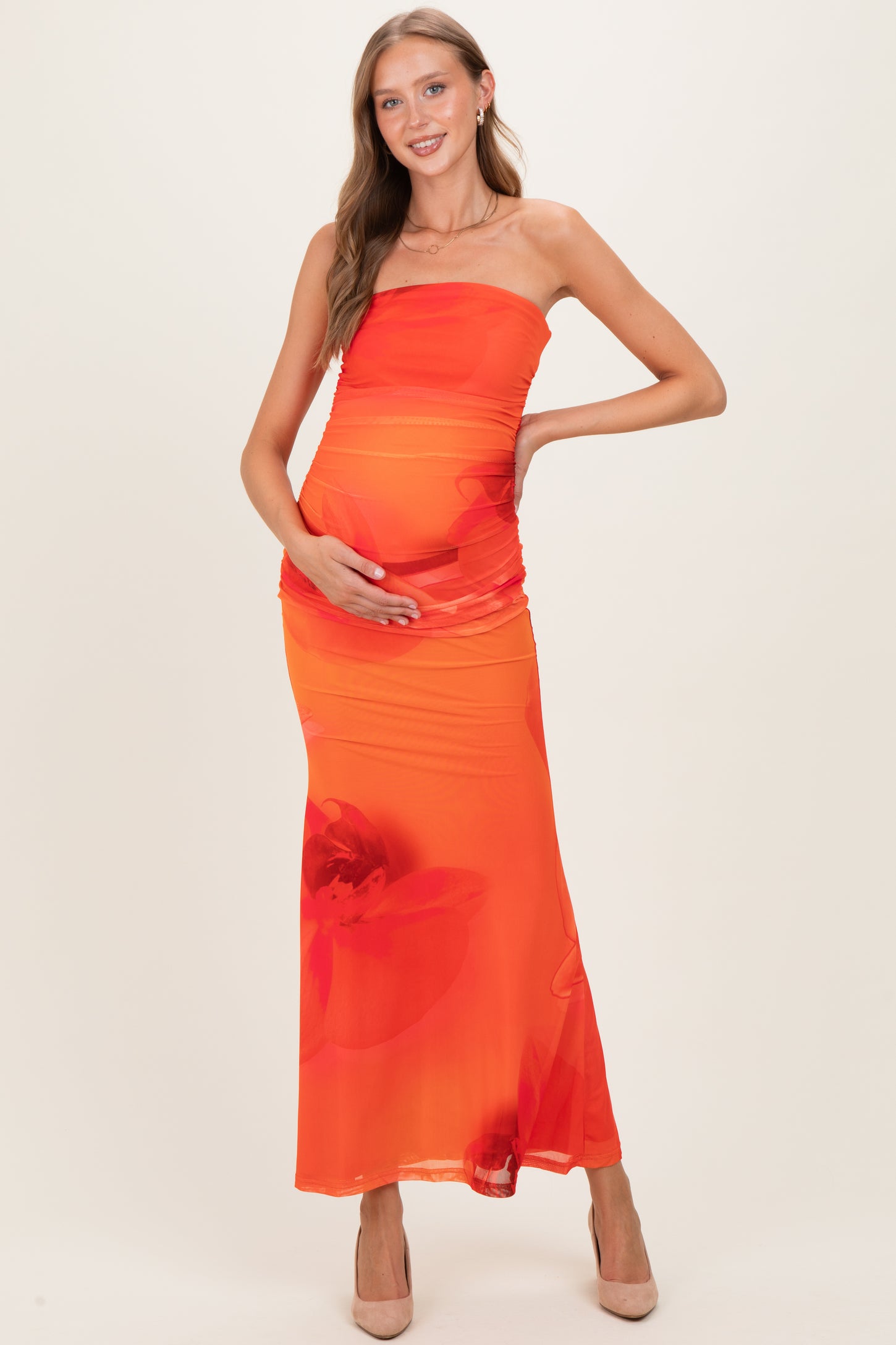 woman wearing a vibrant orange strapless maternity dress with floral patterns, holding her baby bump