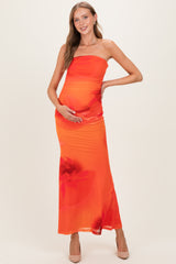 woman wearing a vibrant orange strapless maternity dress with floral patterns, holding her baby bump
