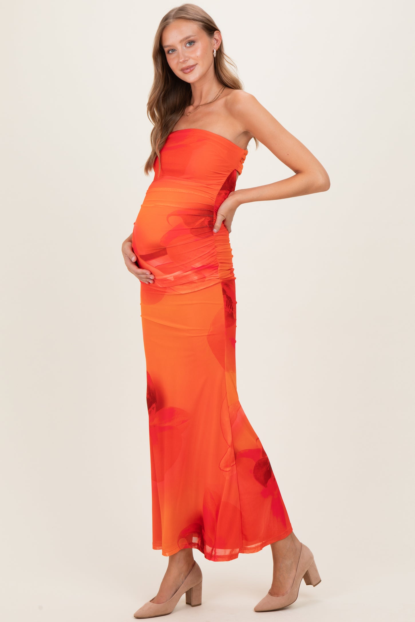 woman wearing an orange maternity dress with floral print and ruching, holding her baby bump