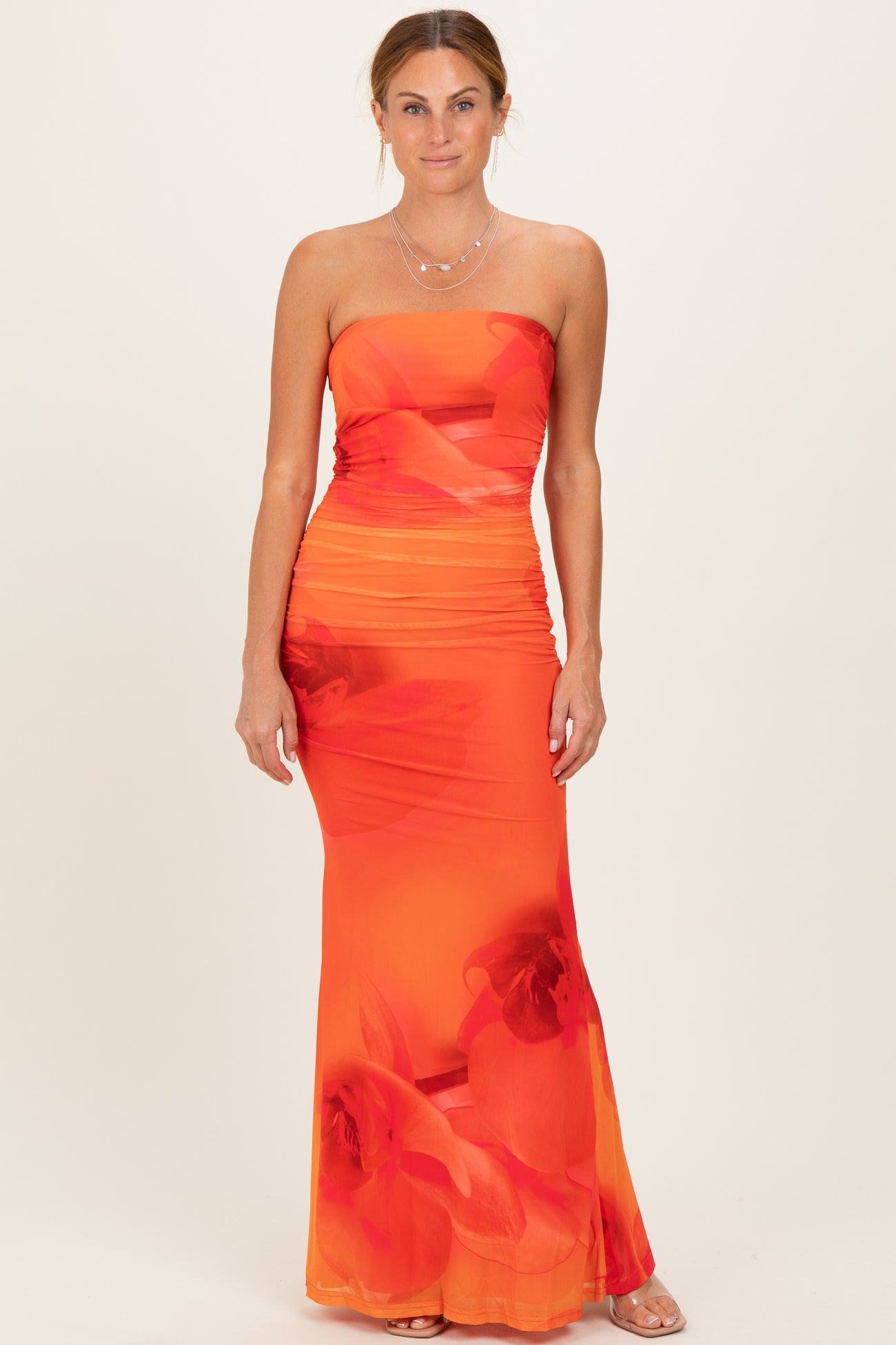 woman wearing a vibrant orange strapless maxi dress with floral print and ruched detailing