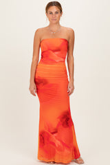 woman wearing a vibrant orange strapless maxi dress with floral print and ruched detailing