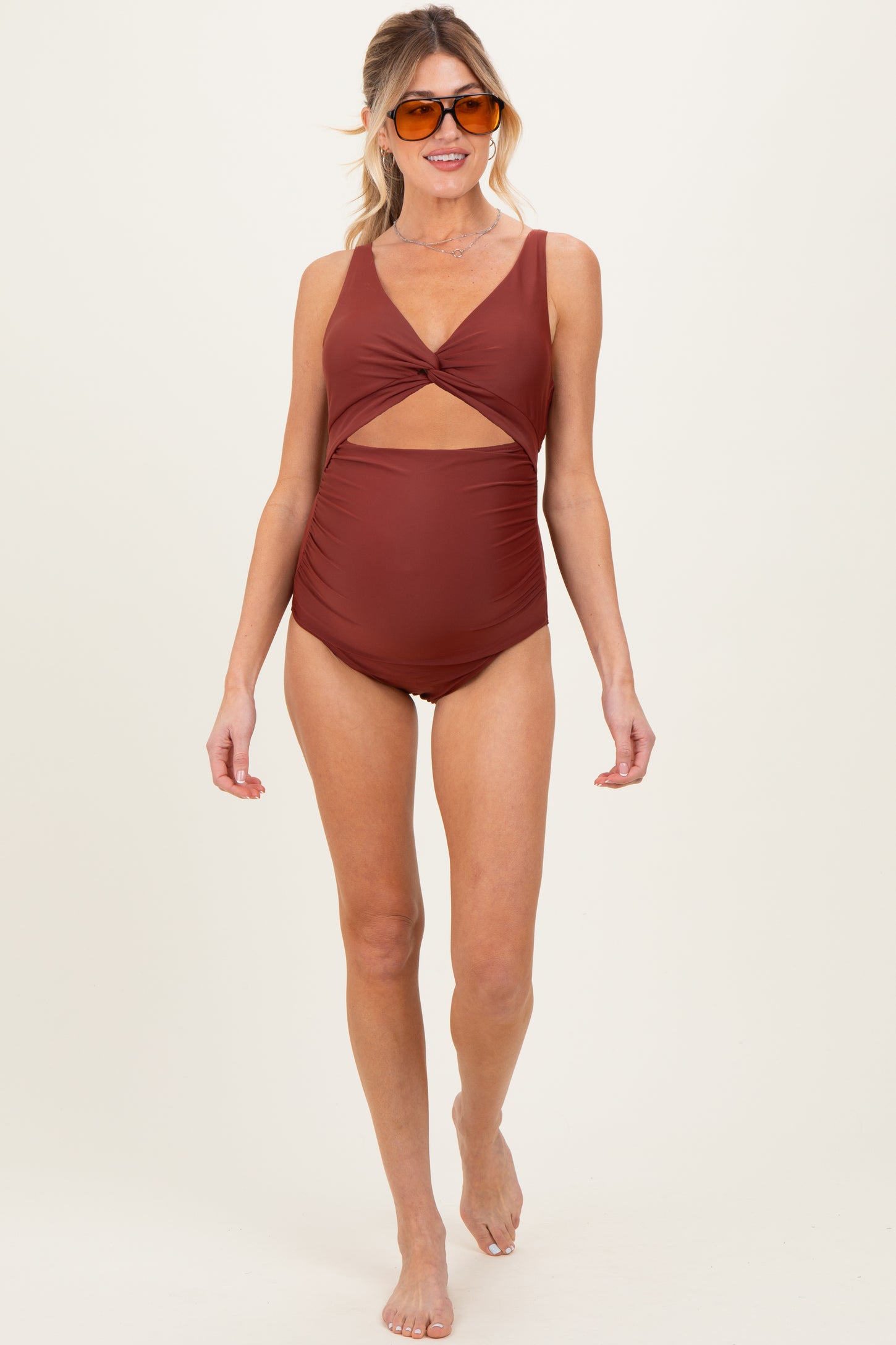woman wearing a rust-colored maternity swimsuit with a cut-out detail and a baby bump visible