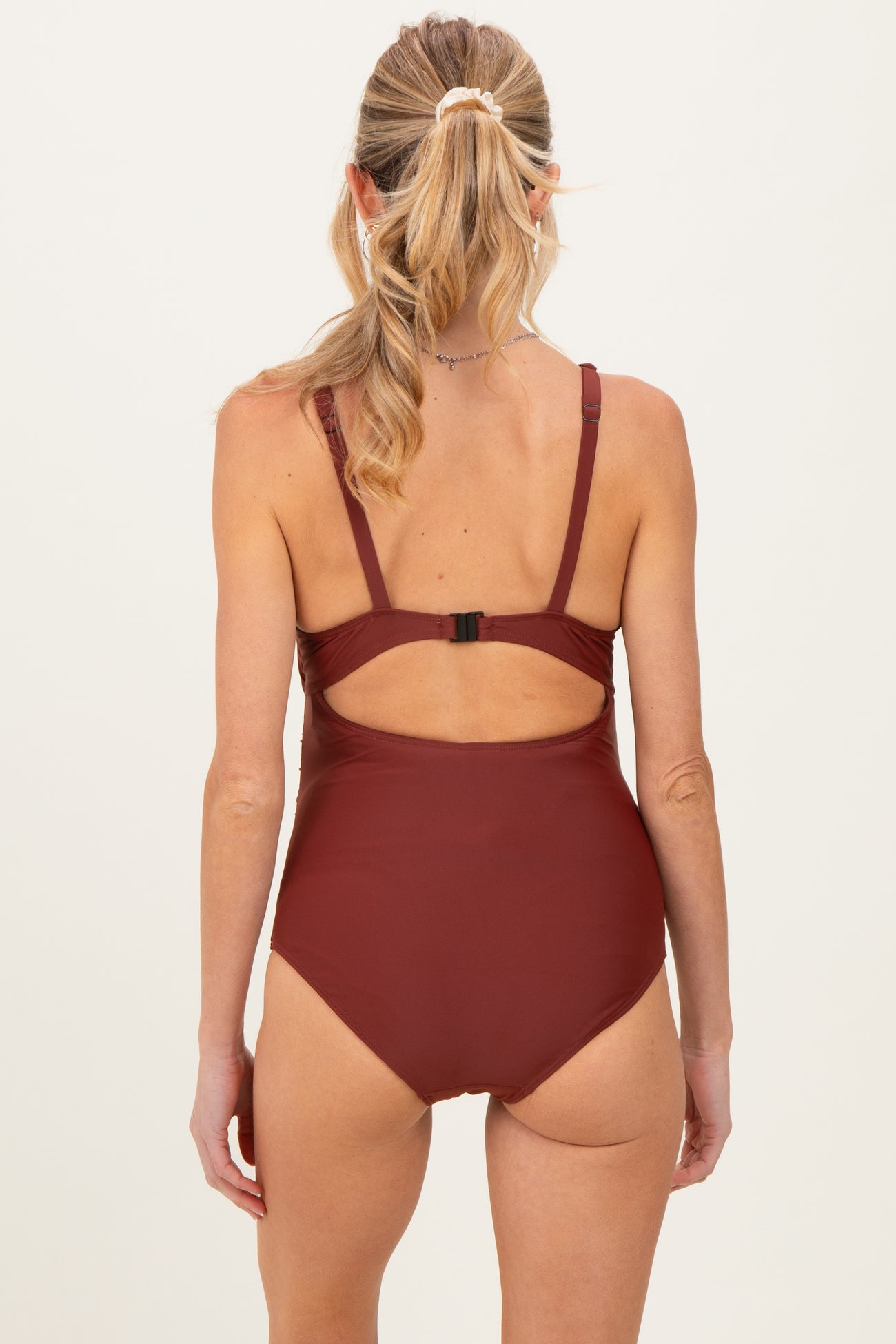 woman wearing a burgundy maternity swimsuit with a back cutout and adjustable straps, showing no visible baby bump