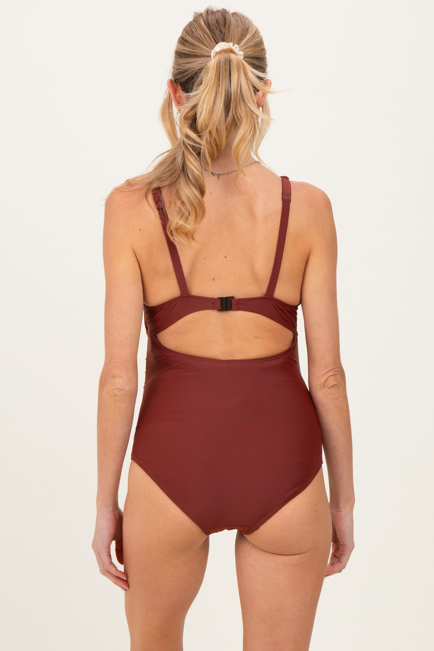 woman wearing a burgundy maternity swimsuit with a back cutout and adjustable straps, showing no visible baby bump