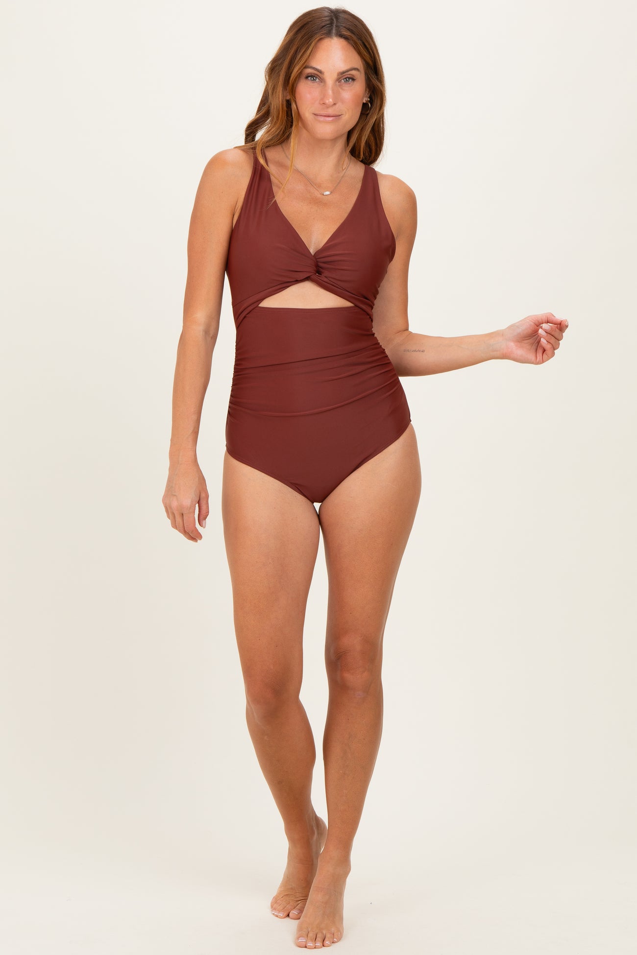 woman wearing a rust-colored one-piece swimsuit with a twist front detail and cut-out sides