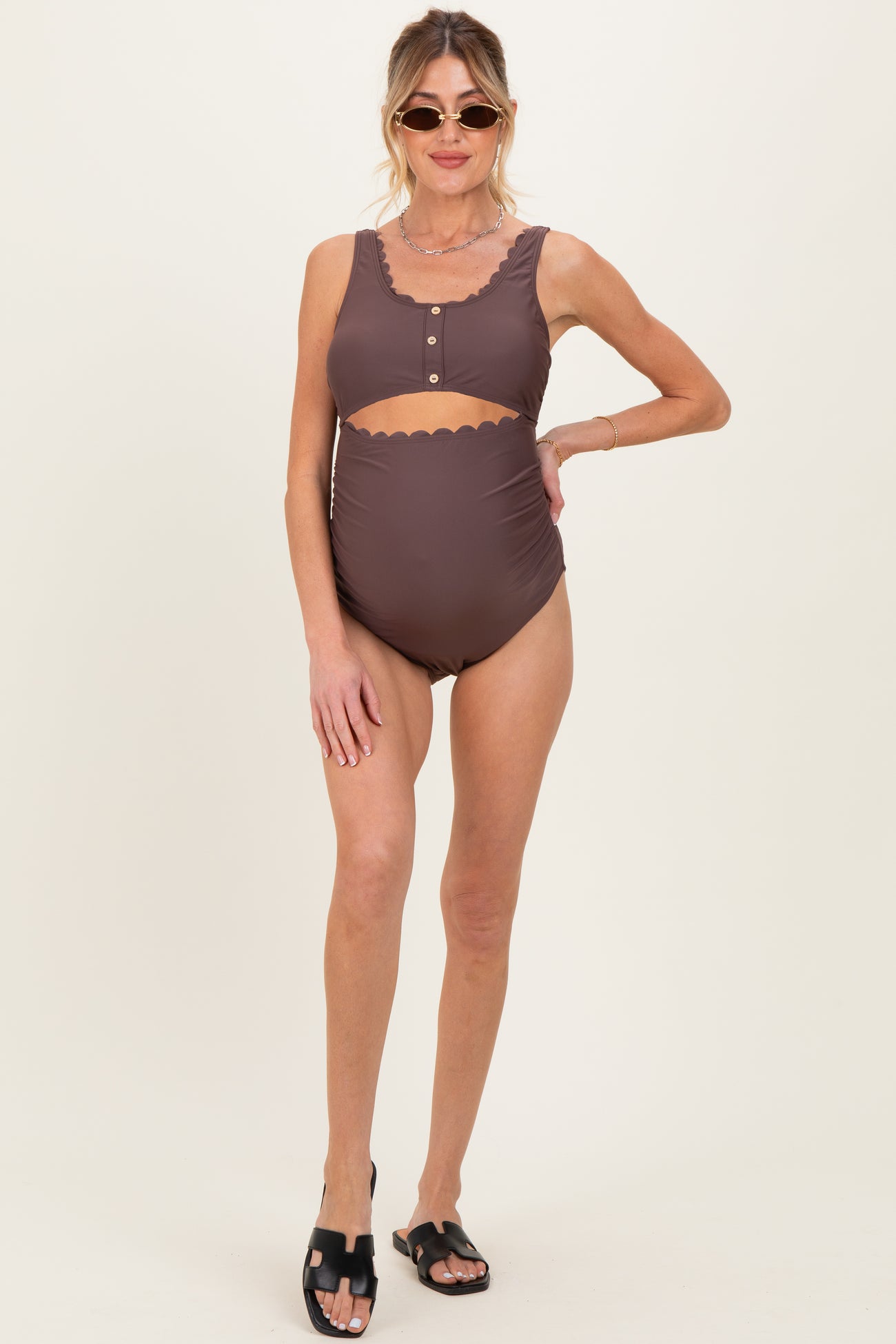 woman wearing a brown maternity swimsuit with scalloped edges and button details, showing her baby bump