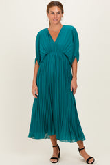 woman wearing a teal pleated midi dress with a deep v-neck and short sleeves, styled with black heeled sandals