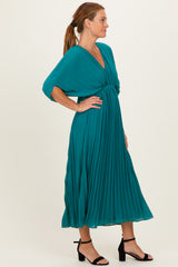 woman wearing a teal pleated midi dress with a deep v-neck and batwing sleeves, styled with black heeled sandals