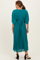 woman wearing a teal pleated midi dress with a cinched waist and batwing sleeves, viewed from the back
