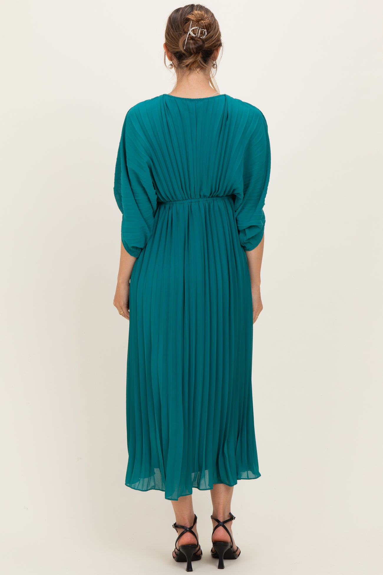 woman wearing a teal pleated maternity dress with a cinched waist and flowy skirt, viewed from the back