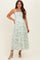 woman wearing a white floral maternity maxi dress with green details and spaghetti straps, posing with a smile