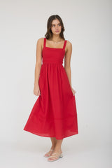 woman wearing a red sleeveless midi dress with a fitted bodice and tiered skirt, standing with one hand on her hip