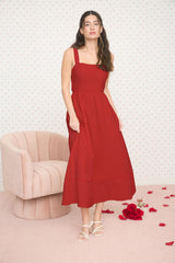 woman wearing a red midi dress with thick straps, standing in a softly decorated room with rose petals on the floor