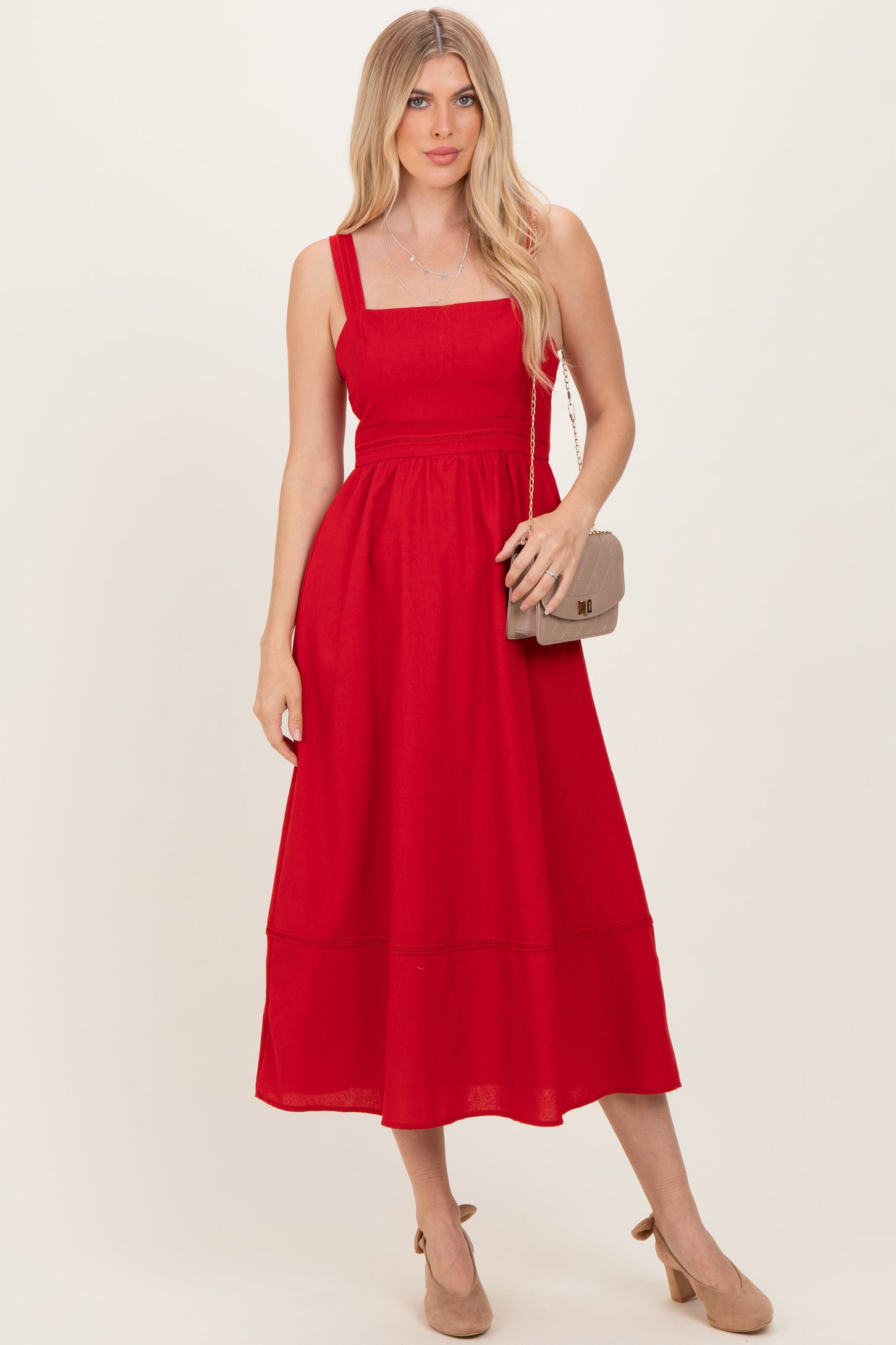 woman wearing a red sleeveless midi dress with a square neckline and a flowy hem, holding a small handbag