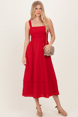 woman wearing a red sleeveless midi dress with a square neckline and a flowy hem, holding a small handbag