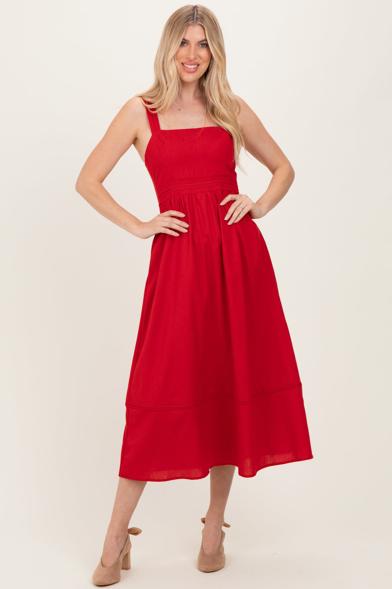 woman wearing a red midi dress with a square neckline and gathered waist, posing with hands on hips