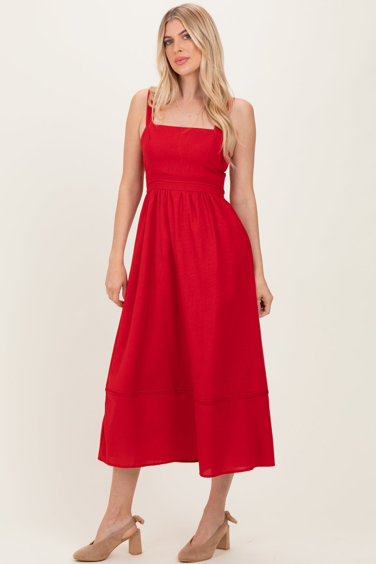 woman wearing a red midi dress with spaghetti straps and a cinched waist, styled with neutral block-heeled shoes