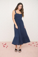 woman wearing a navy blue sleeveless maxi dress with a fitted bodice and ruffle hem, styled with black open-toe heels