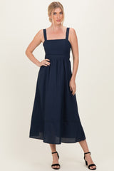 woman wearing a navy blue sleeveless maxi dress with a square neckline and flared skirt, standing confidently