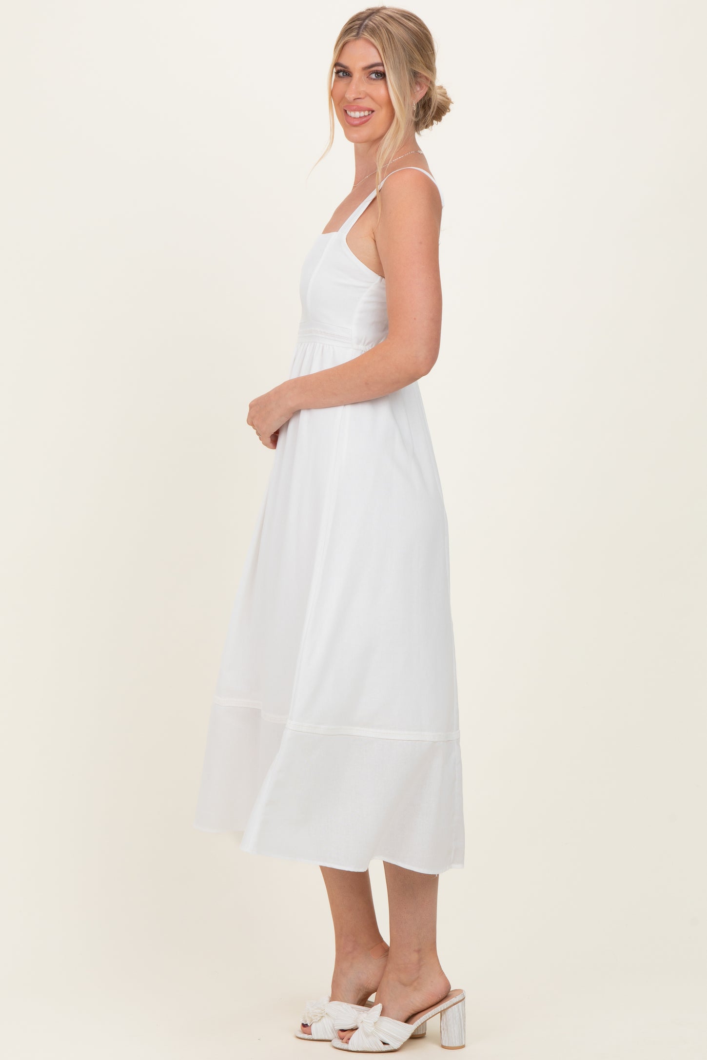 woman wearing a white sleeveless midi dress with a fitted bodice and flowing skirt, styled with open-toe sandals