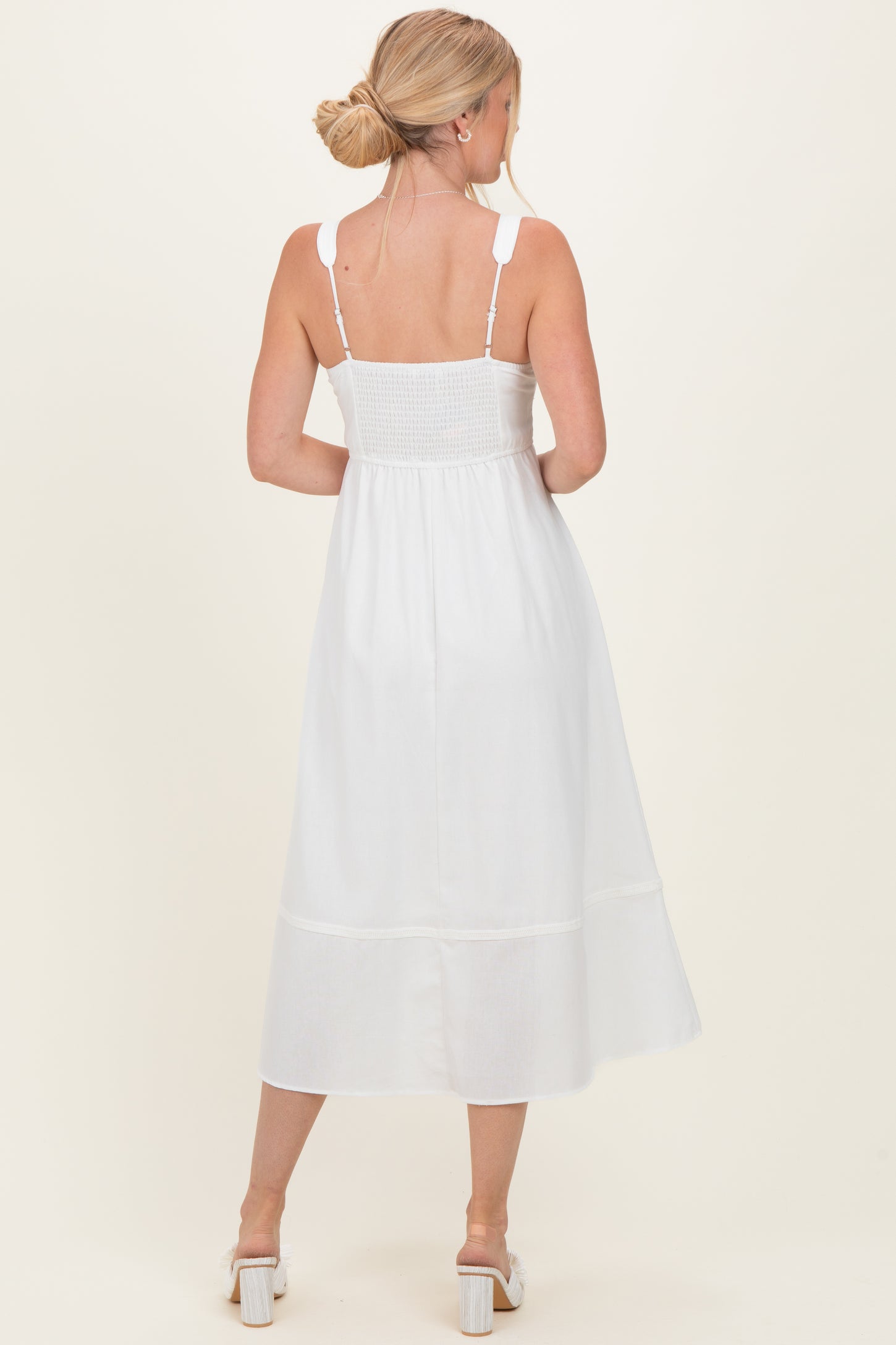 woman wearing a white mid-length sundress with smocked bodice and adjustable straps, shown from the back
