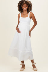 woman wearing a white maternity maxi dress with a square neckline and flowy skirt, holding her baby bump