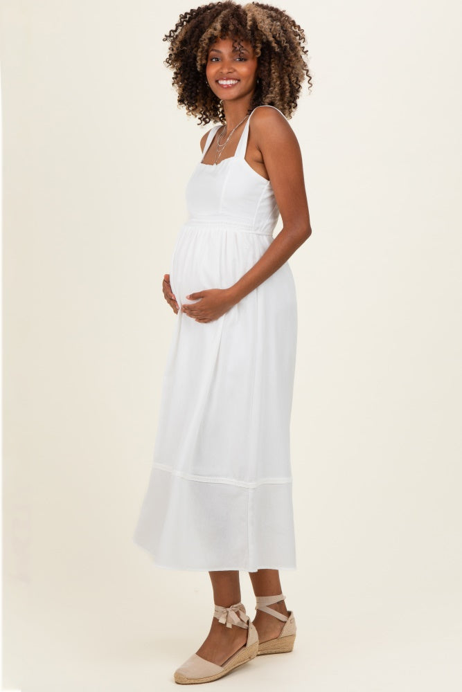 woman wearing a white maternity maxi dress and cradling her baby bump