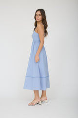woman wearing a light blue spaghetti strap midi dress with a cinched waist and tiered skirt
