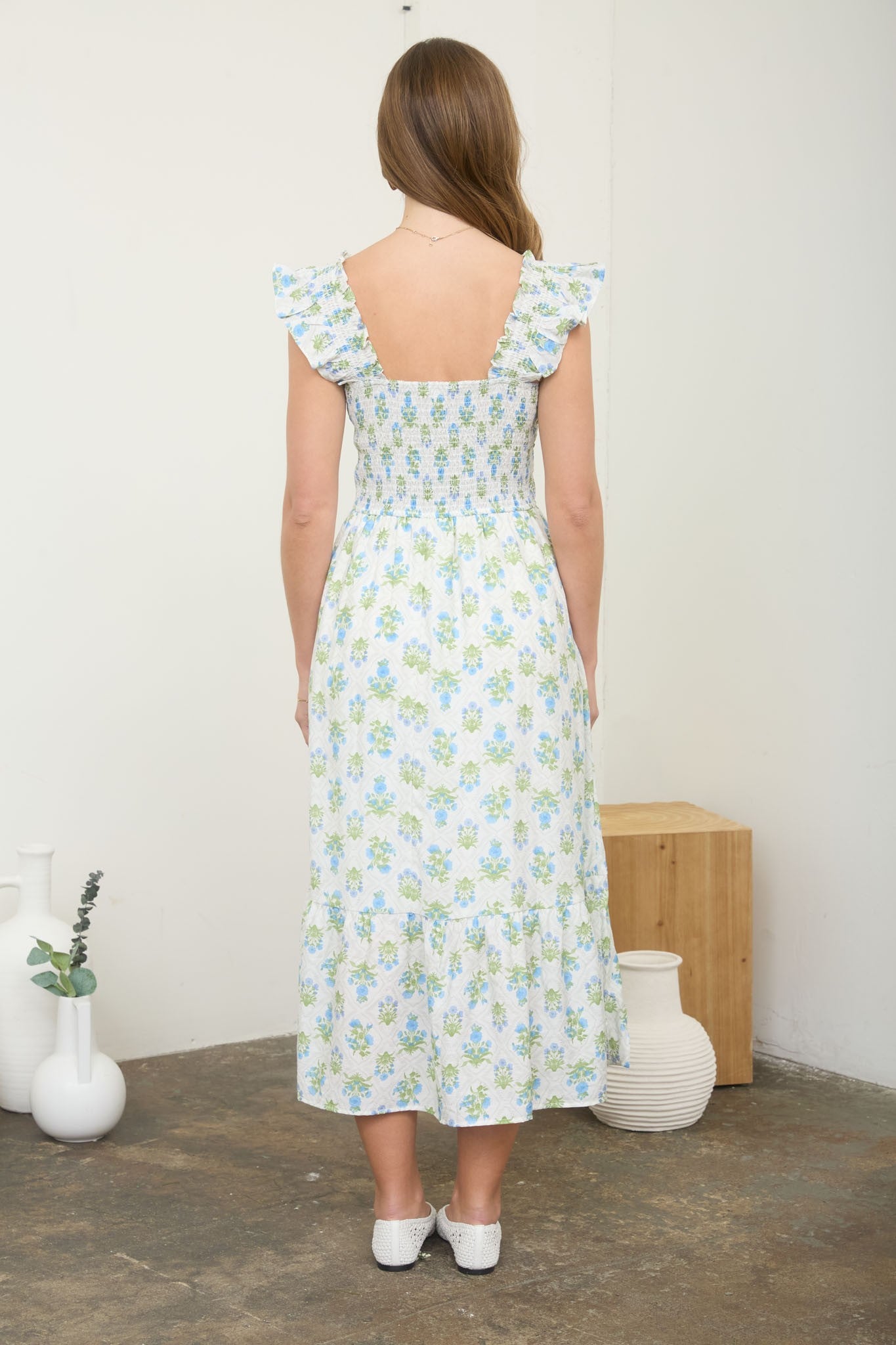 woman wearing a white floral maxi dress with ruffled shoulder straps and a smocked back, standing against a neutral backdrop