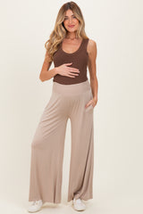 woman wearing a brown ribbed tank top and beige maternity wide-leg pants, holding her baby bump