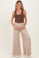 woman wearing a brown ribbed maternity tank top and beige wide-leg maternity pants, holding her baby bump