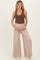 woman wearing a brown ribbed maternity tank top and beige wide-leg maternity pants, holding her baby bump