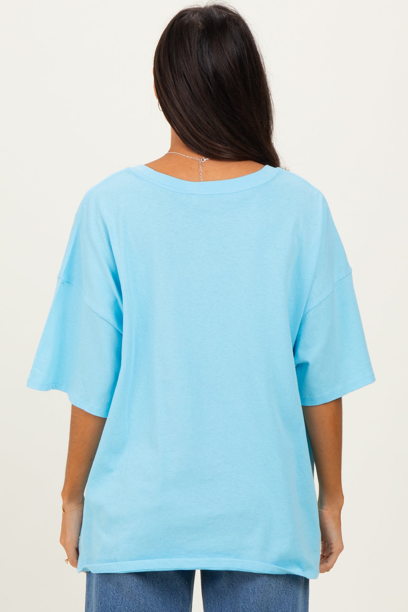 woman wearing a light blue oversized t-shirt viewed from the back, paired with blue jeans