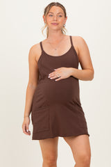 woman wearing a brown maternity dress with adjustable straps and front pockets, holding her baby bump