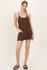 woman wearing a brown sleeveless dress with pockets and a relaxed fit, standing against a light background
