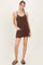 woman wearing a brown sleeveless dress with pockets and a relaxed fit, standing against a light background
